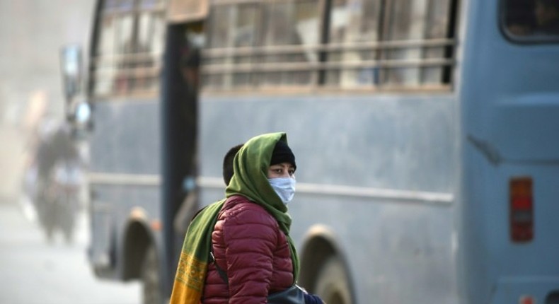 A woman covers her face with a mask as she walks along a dusty road in Kathmandu