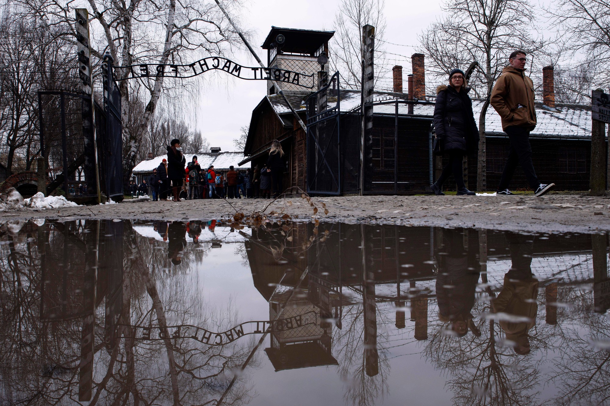 Ľudia kráčajú okolo nápisu pri vstupe do bývalého nacistického koncentračného tábora Auschwitz-Birkenau v poľskom Osvienčime 26. januára 2023.