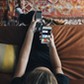 High angle view of teenage girl using phone app and remote control while sitting on sofa watching TV