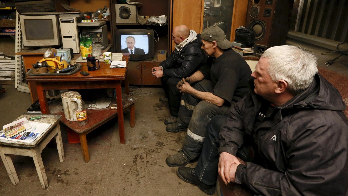 Workers watch a TV broadcast of Russian President Putin address to the Federal Assembly at an auto r