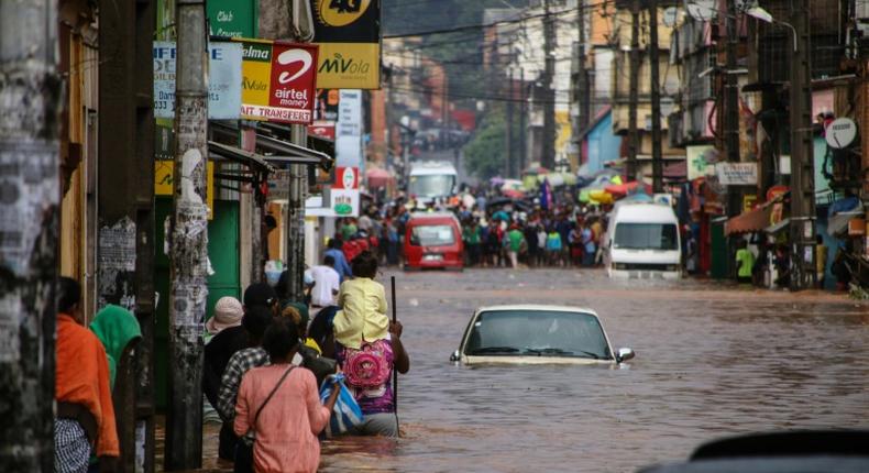 Residents walk through floodwaters past submerged vehicles on a road in the capital Antananarivo