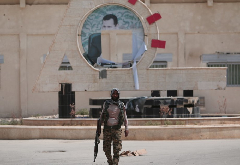 A Kurdish fighter from the People's Protection Units (YPG) carries his weapon as he walks at the faculty of economics where a defaced picture of Syrian President Bashar al-Assad is seen in the background, in the Ghwairan neighborhood of Hasaka