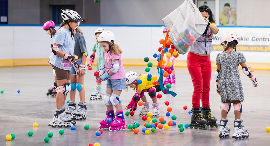 Dzieci bawią się i uczą jeździć na rolkach pod okiem instruktorów