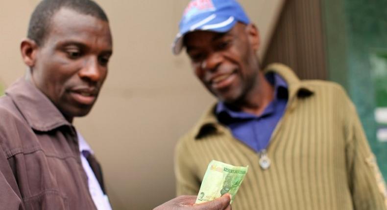 Two men look at a bond note released by the Reserve Bank Of Zimbabwe in the capital Harare