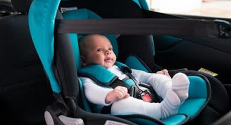 A baby strapped into a car seat, inside a car