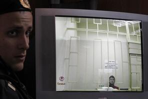 A bailiff stands next to a screen with a live broadcast of a court hearing an appeal by an oppositio