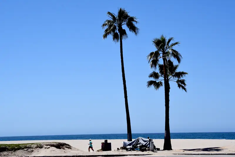 Opustoszały z powodu pandemii bulwar Venice Beach, biegacz mija namiot bezdomnego, 21 kwietnia 2020