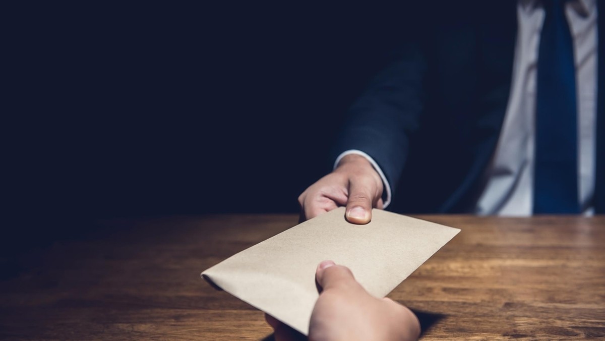 A man giving bribe money in a brown envelope to another businessman in the dark