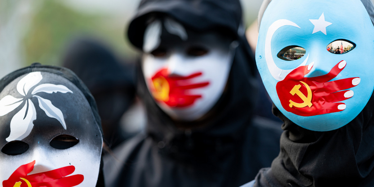 Grupa protestujących nosi maski symbolizujące uciszenie przez Komunistyczną Partię Chin ujgurskich muzułmanów i ruch prodemokratyczny w Hongkongu. Hongkong, 2019 r.