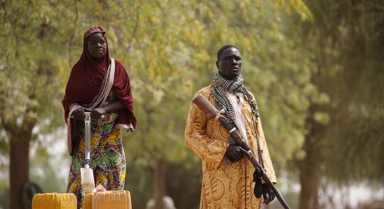 A member of a civilian vigilante group holds a hunting rifle while a woman pumps water into jerrycans in Kerawa, Cameroon, March 16, 2016. 