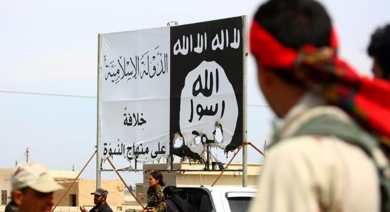 Members of the US-backed Syrian Democratic Forces stand under an Islamic State group banner in the recently recaptured town of Al-Karamah, near the IS bastion of Raqa