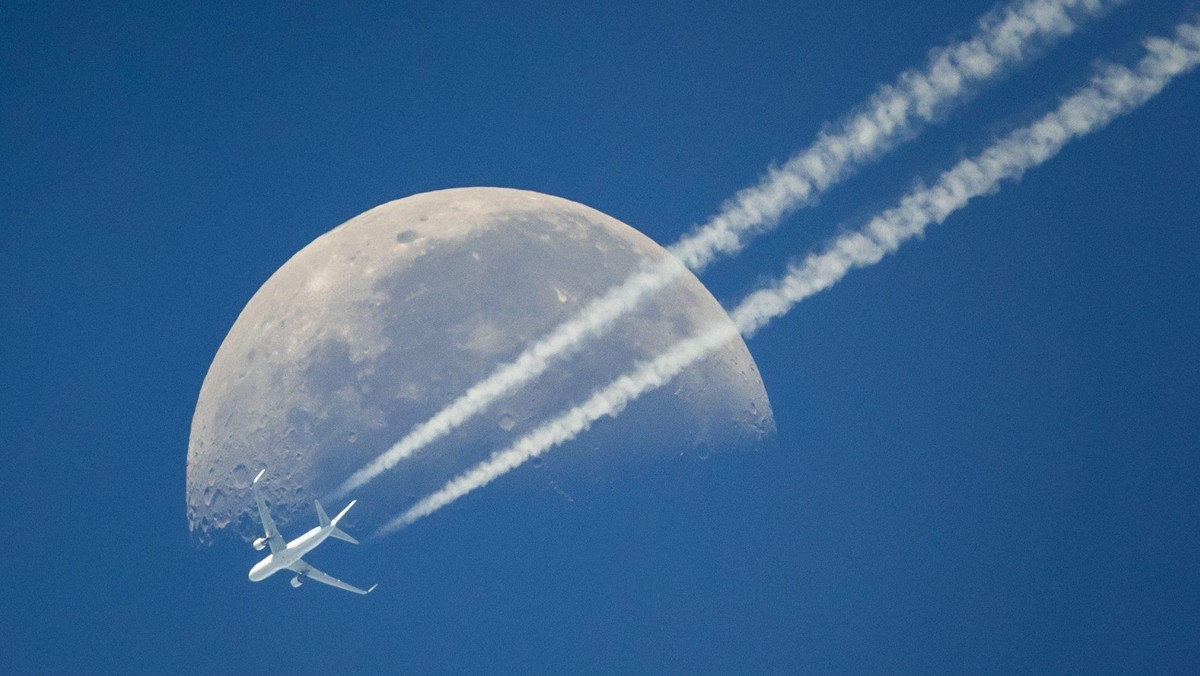 A commercial airplane flies past the moon above Geneva