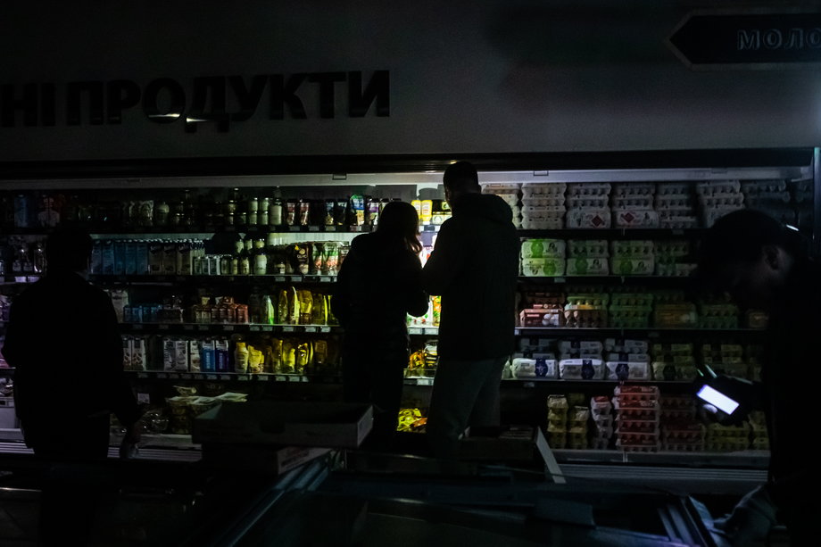 Zakupy w dziale spożywczym supermarketu podczas przerwy w dostawie prądu w Kijowie. Kupujący oświetlają towary telefonami komórkowymi. 27 października 2022 r. 