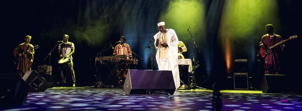 <strong>Balla Kouyaté</strong>
<br></br>
Kolejną gwiazdą wieczoru był wirtuoz balafonu. Balla Kouyaté gra na dwóch balafonach jednocześnie, co zdarza się bardzo rzadko. Balafon to instrument przypominający ksylofon, jednak bardziej surowy w brzmieniu, a na dodatek Balla Kouyaté potrafi z niego wydobyć zaskakujące dźwięki. Towarzyszyli mu muzycy grający na kilku innych afrykańskich i europejskich instrumentach perkusyjnych oraz na gitarach, a także wokalista wykonujący dawne pieśni.
<br></br>
fot. Mateusz Bral
<br></br>