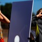 A reflected image of the sun is seen on a white board as kids look up to view the beginning a partia