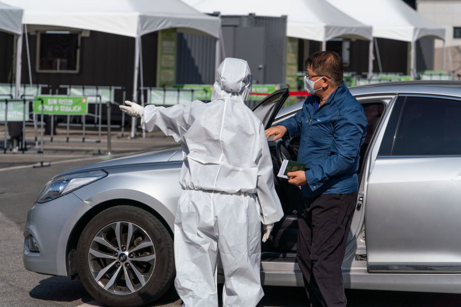W Korea Południowej istnieją też mobilne centra do testowania, do których przyjeżdża się samochodami. Na zdjęciu: pracownik laboratorium kieruje pacjenta do jednego z punktów testowania.