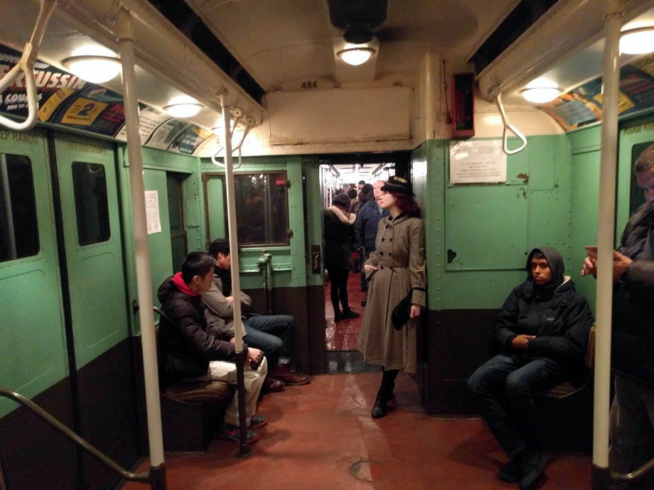 A woman dressed in early 20th-century fashion (while listening to music on her 21st-century smartphone) on the annual Shopper's Special subway line.
