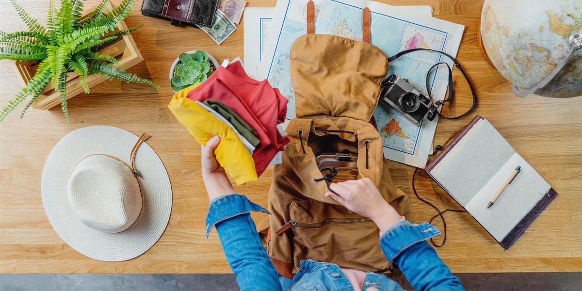 Top view of young woman packing for vacation trip holiday, desktop travel concept.