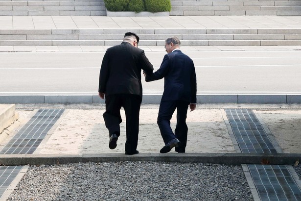 Najwyższy przywódca Korei Północnej Kim Dzong Un i prezydent Korei Południowej Mun Jae-in trzymają się za ręce, przechodząc symbolicznie przez linię demarkacyjną w strefie zdemilitaryzowanej pomiędzy dwoma krajami