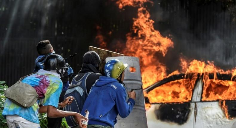 Anti-government demonstrators take cover behind shields near a burning car during clashes near Altamira Square in Caracas, on June 14, 2017