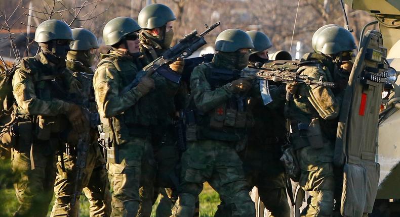 Armed men, believed to be Russian servicemen, take cover behind an armoured vehicle as they attempt to take over a military airbase in the Crimean town of Belbek near Sevastopol March 22, 2014.