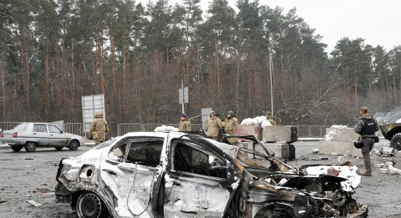 Ukrainian servicemen and volunteers of Ukraine's Territorial Defense Forces stand behind a damaged car at a checkpoint in Brovary, outside Kyiv, Ukraine, Tuesday, March 1, 2022.