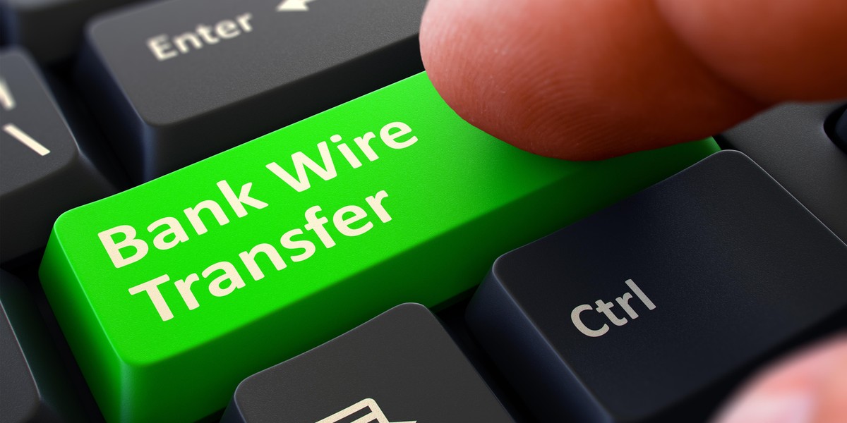 Pressing Green Button Bank Wire Transfer on Black Keyboard.