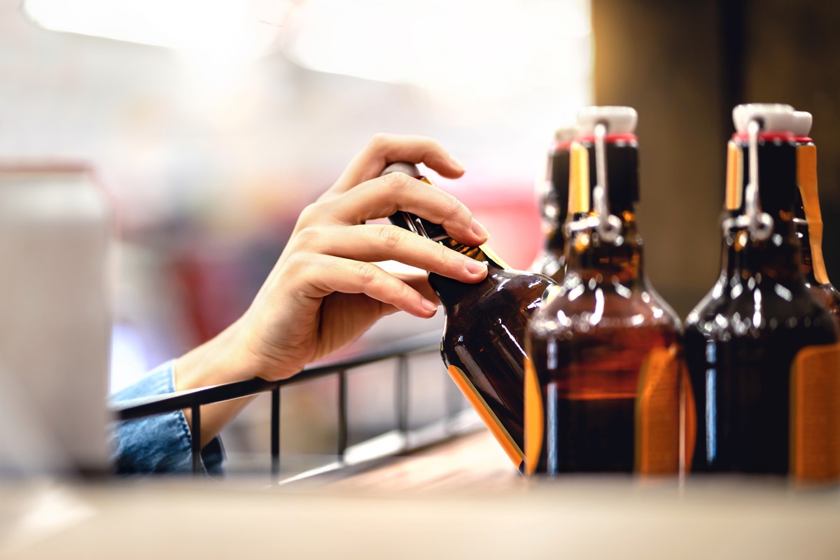 człowiek wyciąga rękę po butelki alkoholu stojące na sklepowej półce