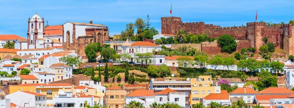 <strong>Poczuj klimat prawdziwej Portugali w Silves</strong>
<br></br>
Leżące nieopodal Faro Silves, to jedno z najstarszych tutejszych miast, które w czasie gdy region znajdował się pod okupacja Maurów, było stolicą regionu. Dziś jest to miejsce, które przypomina głównie o czasach panowania muzułmanów i sięga VIII wieku. Nie ma tu zbyt wielu turystów – głównie dlatego, że do morza jest stąd około piętnastu kilometrów. Warto jednak odwiedzić to miejsce, ponieważ pozwala poczuć klimat dawnej Portugalii. 
Znakiem rozpoznawczym Silves jest czerwony zamek - fortyfikacja została wzniesiona przez Maurów w VII wieku i mimo upływu czasu oraz burzliwej historii, budowla przetrwała w zaskakująco dobrym stanie. Do dziś góruje nad całym miasteczkiem, przypominając o jego dziejach, ale też zapewniając doskonały widok na całą okolicę. 
<br></br>
Przy okazji wizyty w tym miejscu można udać się też do pobliskiego Ferragudo – małego, rybackiego miasteczka, położonego naprzeciw Portimão. Tutaj, na świeżym powietrzu restauracje serwują świeżo złowione z grilla sardynki. W okolicy znajduje się też przepiękna Praia da Rocha – piękno tej plaży docenicie zwłaszcza o zachodzie słońca, kiedy to skały wypiętrzające się pośród piasku mienią się w różnych odcieniach czerwieni. 
<br></br>
<a  href=
