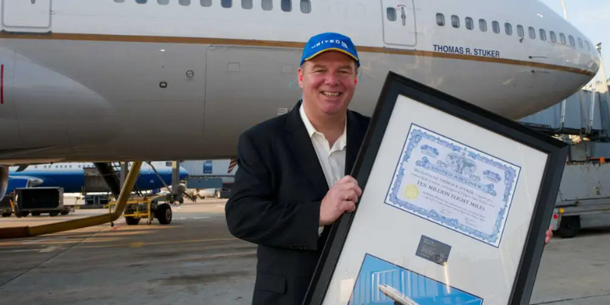 Tom Stuker odbierający pamiątkowy dyplom po przekroczeniu 10 mln mil w powietrzu. W tle samolot United Airlines nazwany jego imieniem.