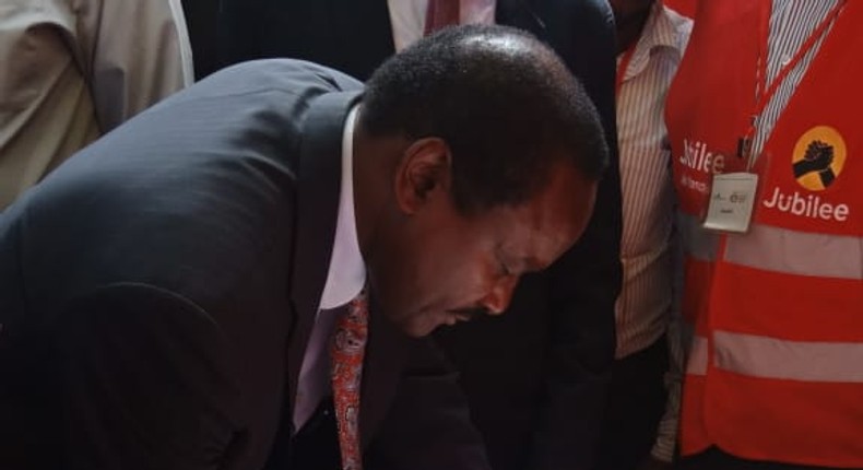 Wiper party leader Kalonzo Musyoka signs the visitor's book at a Jubilee party stand during the  People's Democratic Festival (Twitter)