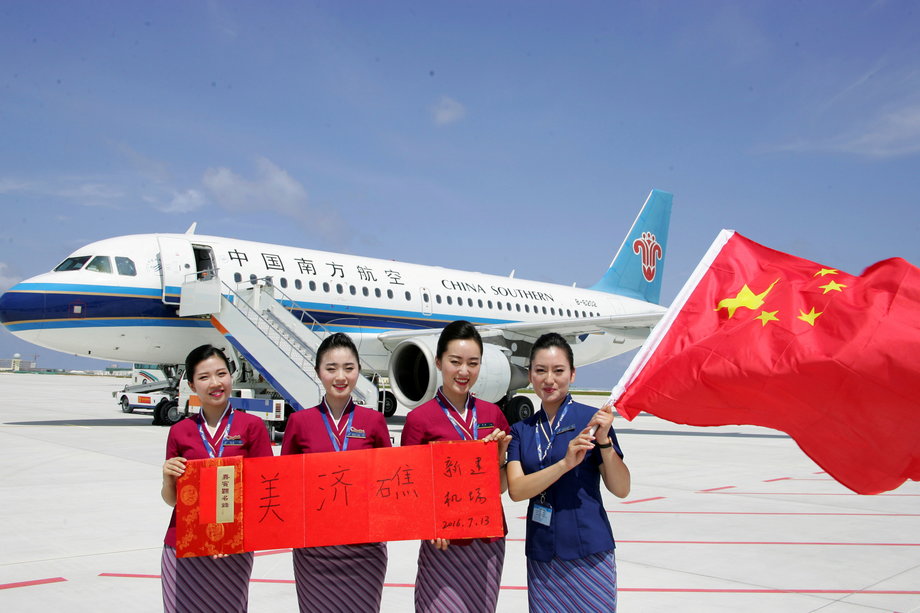 Crew members holding a Chinese national flag pose in front of a plane at a new airport China built on Mischief Reef in the South China Sea.