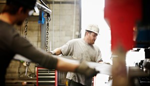 Steel workers placing sheet steel in a large brake pressThomas Barwick/Getty Images