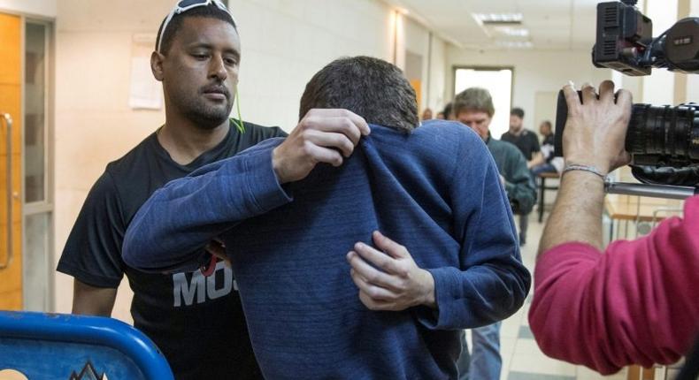 A US-Israeli Jewish teenager accused of making dozens of anti-Semitic bomb threats in the United States and elsewhere is escorted by guards as he leaves an Israeli court after his arrest
