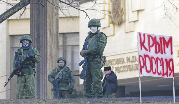 Symferopol w 2014 r. Uzbrojeni mężczyźni stoją przed budynkiem lokalnego parlamentu, w tle transparent z napisem „Krym to Rosja”