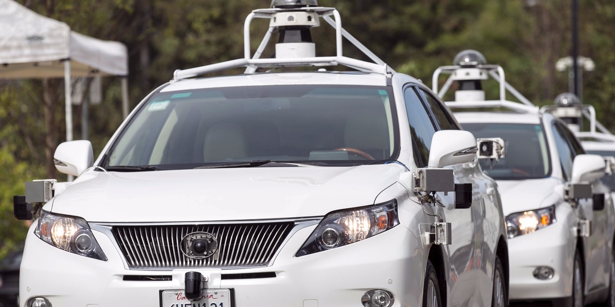 A line of Lexus SUVs equipped with Google self-driving sensors await test riders during a media preview.