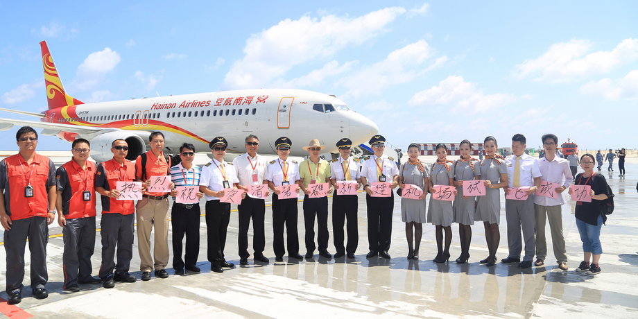 Crew members stand in front of a plane of Hainan Airlines.