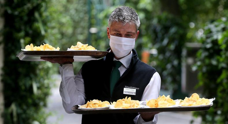 A waiter with a face mask carries food in a restaurant in Vienna, Austria, Thursday, May 14, 2020. In Austria restaurants may open again under certain conditions from Friday on. The Austrian government has moved to restrict freedom of movement for people, in an effort to slow the onset of the COVID-19 coronavirus. (AP Photo/Ronald Zak)