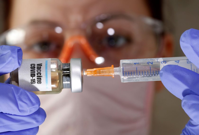 A woman holds a small bottle labbeled with a "Vaccine COVID-19" sticker and a medical syringe in thi