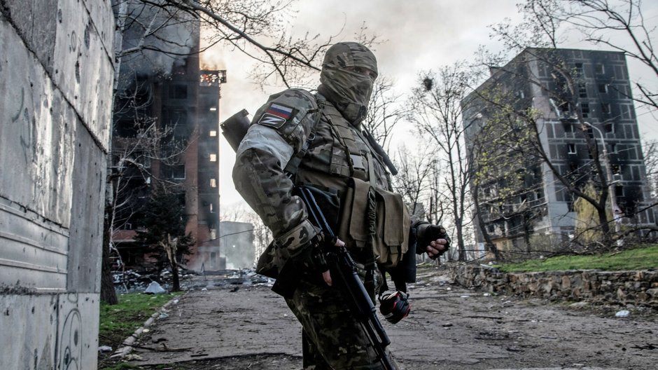 Rosyjski żołnierz stoi na tle płonącego bloku mieszkalnego w centrum Mariupola. Ukraina, 18.04.2022