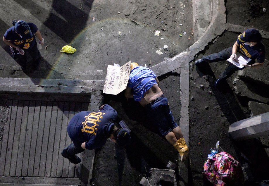 Police officers inspect the body of a man who police said was a victim of a drug-related vigilante execution in Manila. The cardboard found near his body reads: "Kage Lao, drug lord from Mindanao. You are next."