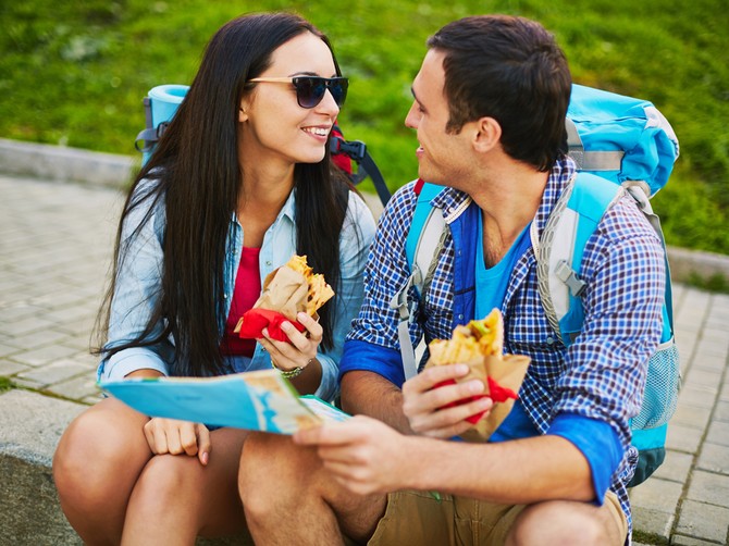 114347_stockphotohappytravelerssmilingononeanotherwhilesittingonpavementandeatingfastfood219258595