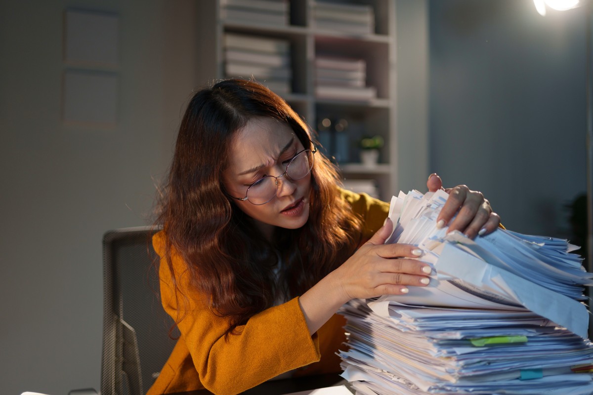 Kobieta w okularach przegląda stos dokumentów.