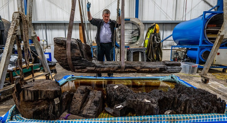 Researcher lifts up coffin containing the remains of a man and a perfectly preserved axe.
