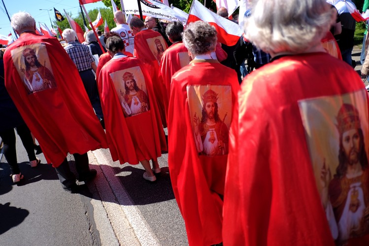 Uczestnicy marszu śpiewają pieśni religijne, kilkanaście osób niesie duży krzyż.