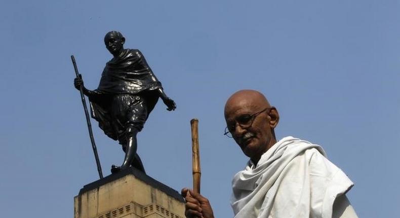 Mahesh Chaturvedi, 63, who dresses up like Mahatma Gandhi, poses for a photo in front of a statue of Gandhi in the old quarters of New Delhi October 25, 2012. 