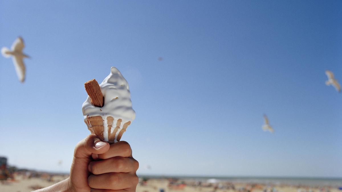 Man holding ice cream on beach, close-up of hand