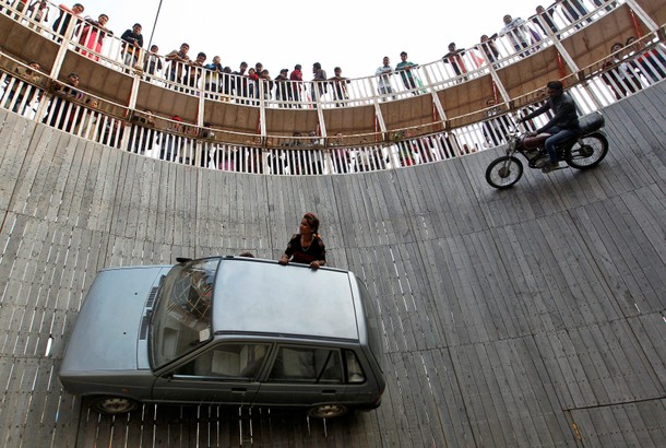 Stunt performers ride a motorcycle and a car on the walls of the Well of Death at the Magh Mela fa