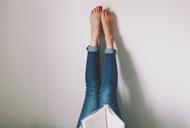 Woman Lying On Bed Reading Book With Legs Raised