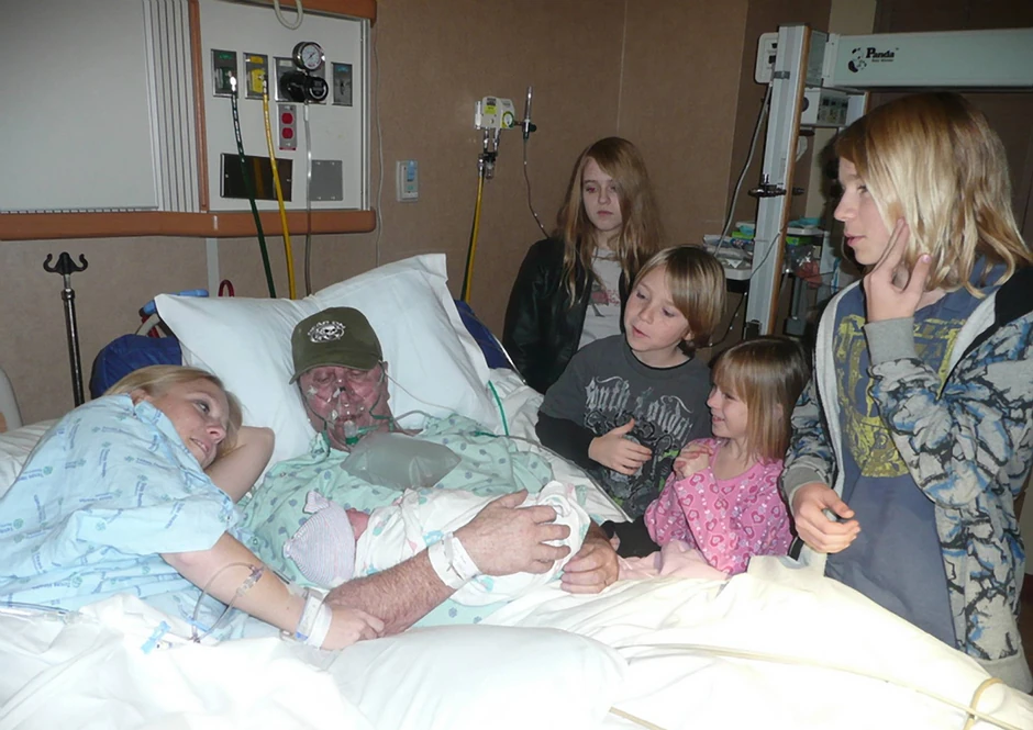 Cela porodica Aulger pored Marka koji drži bebu u bolničkoj postelji